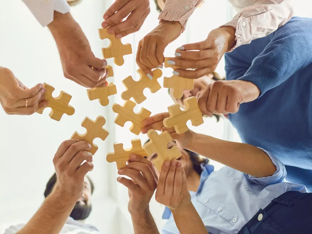 A diverse group of people holding wooden puzzle pieces together, symbolizing collaboration and connection in ADHD couples group therapy