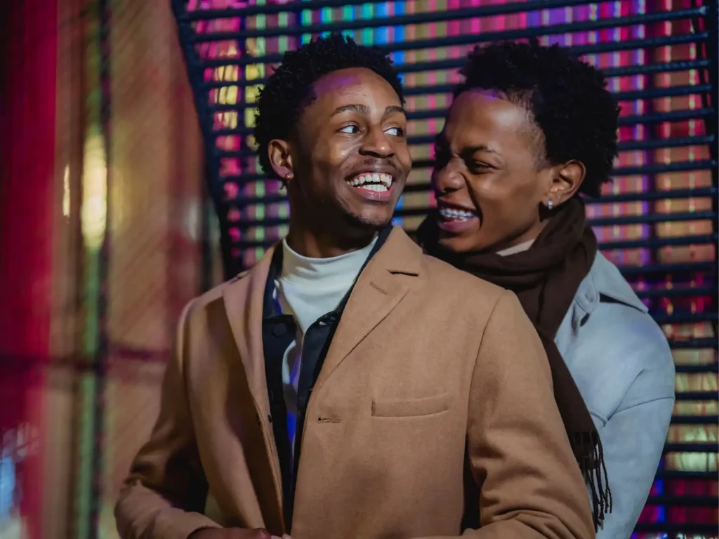 A joyful LGBTQ+ couple embraces and laughs together in front of vibrant, colorful lights, representing the deep emotional bonds nurtured through Emotionally Focused Therapy (EFT) in Los Angeles.