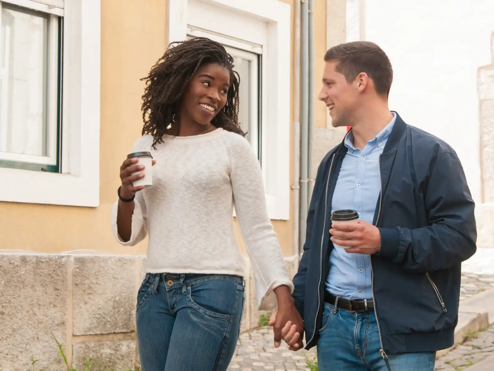 A happy couple holding hands and sharing coffee on a charming city street, embodying the warmth and connection nurtured in couples therapy with Grazel Garcia in Los Angeles.