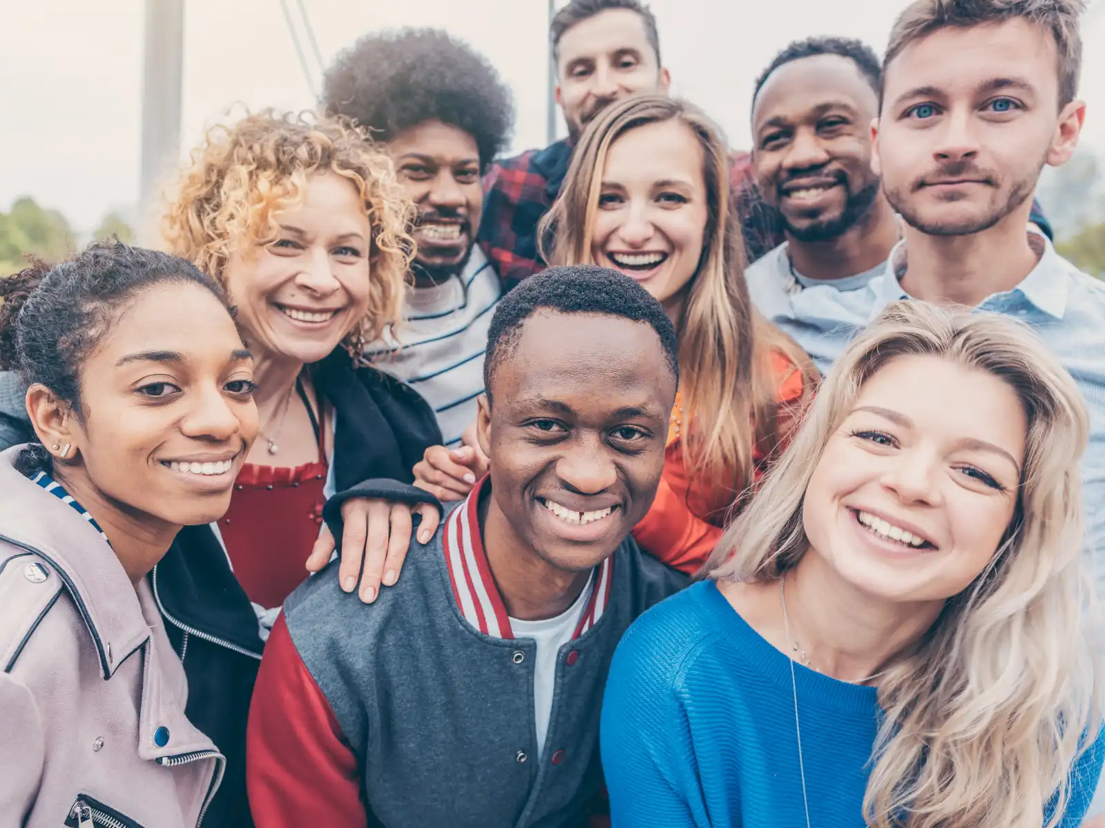 A diverse group of people smiles and poses together outdoors, radiating warmth and connection. The image captures a sense of community, friendship, and mutual support—perfect for illustrating group therapy in Los Angeles.