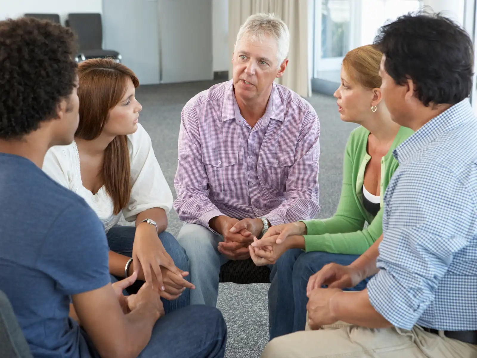 A group of adults engaged in a heartfelt discussion in a therapy session, emphasizing open communication and emotional support in a healthy relationships group therapy setting.
