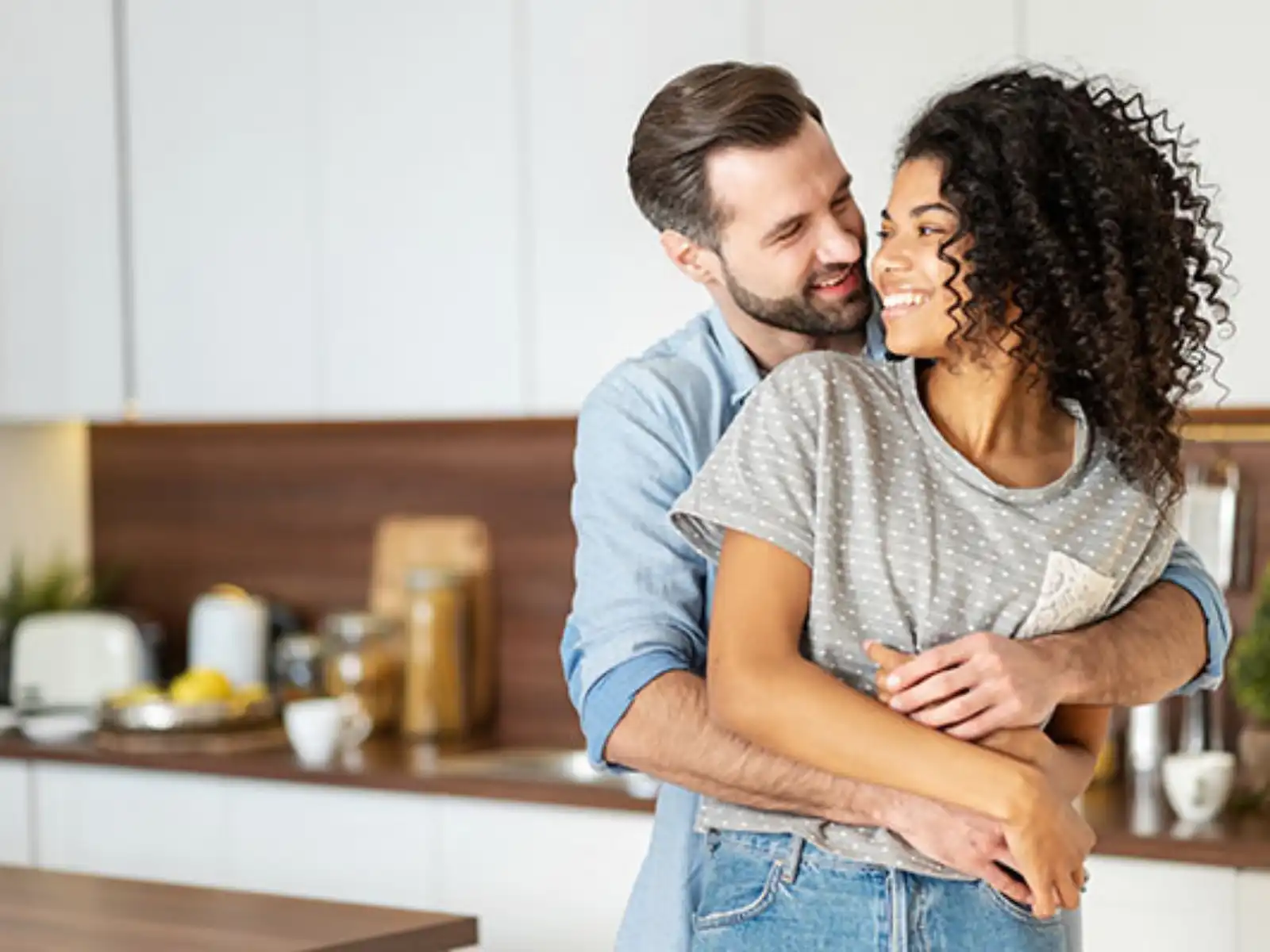 A happy interracial couple embraces in a warm and loving moment in their kitchen, reflecting the connection and understanding fostered through interracial couples therapy in Los Angeles.