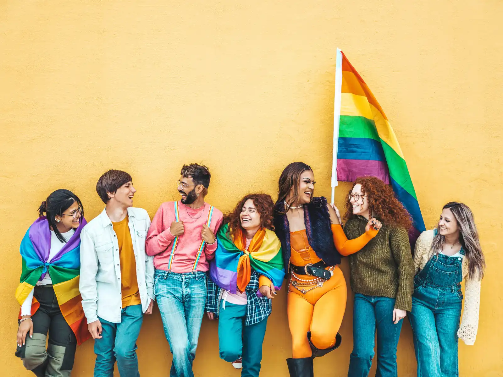 A joyful group of LGBTQ+ individuals stands together, wrapped in pride flags and sharing laughter, symbolizing the support and inclusivity fostered through LGBTQ+ couples therapy in Los Angeles.