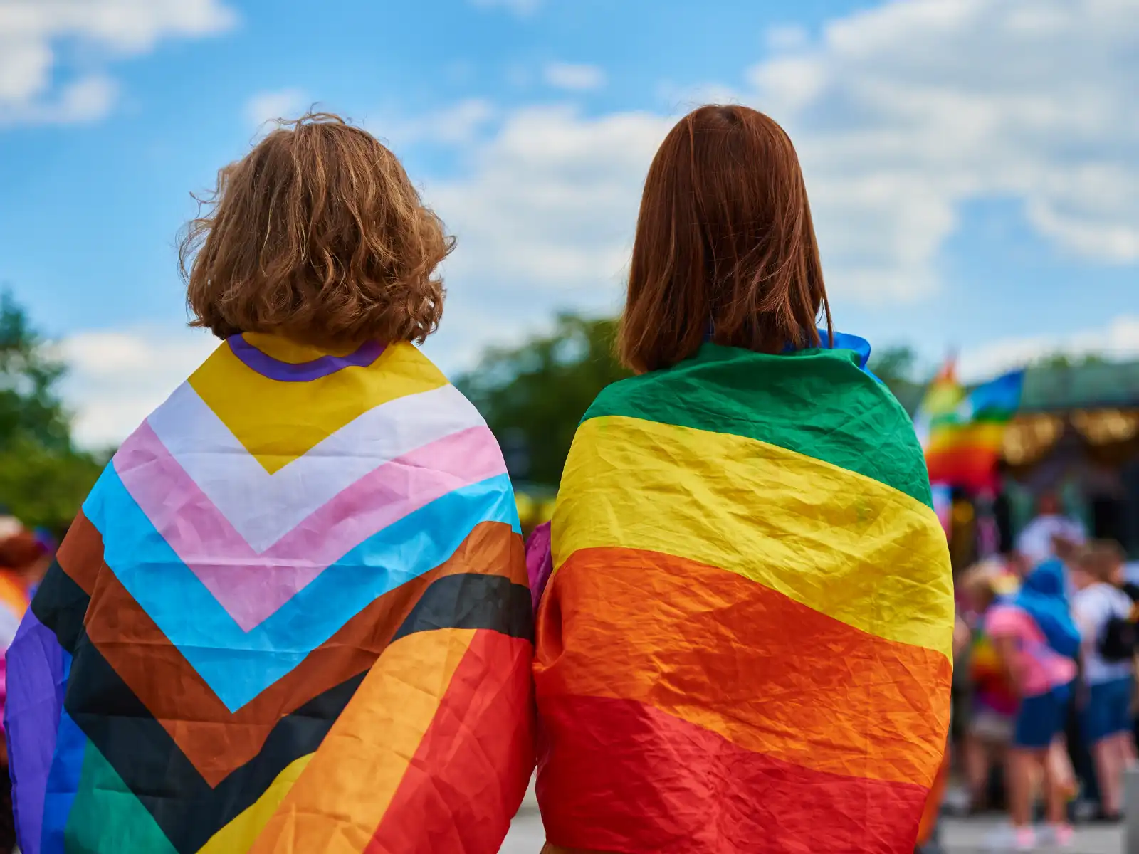 Two individuals draped in LGBTQ+ pride flags stand together at an outdoor event, symbolizing community, acceptance, and the inclusive support of LGBTQ+ therapy in Los Angeles.