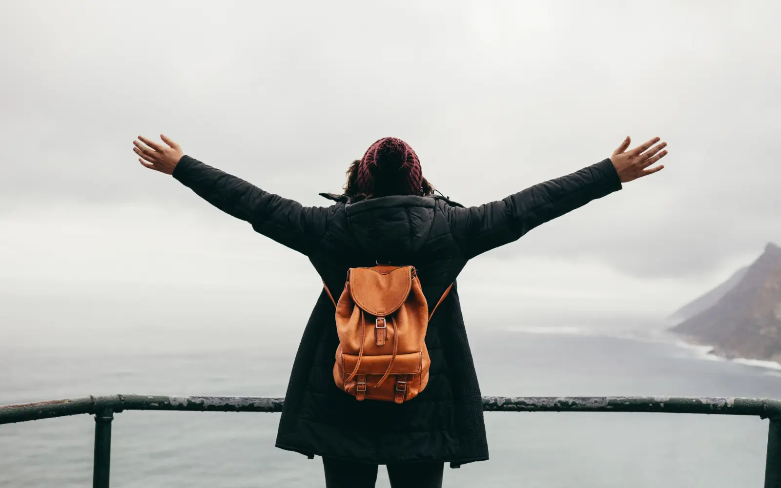 A woman standing on a cliff top with her arms open wide looking out over the sea symbolizing the Freedom you can achieve through individual therapy