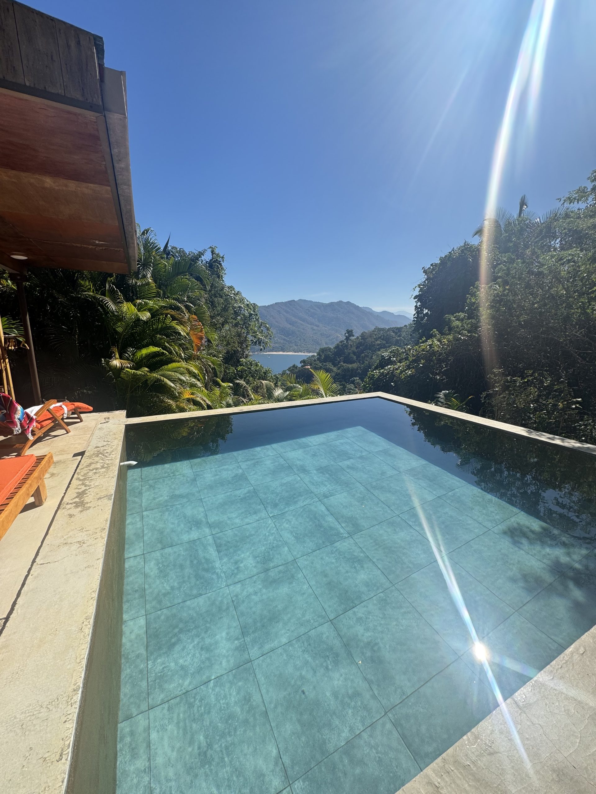 Infinity pool with crystal-clear water overlooking lush greenery and distant mountains, with a glimpse of the ocean. A serene and luxurious retreat setting designed for relaxation and connection.