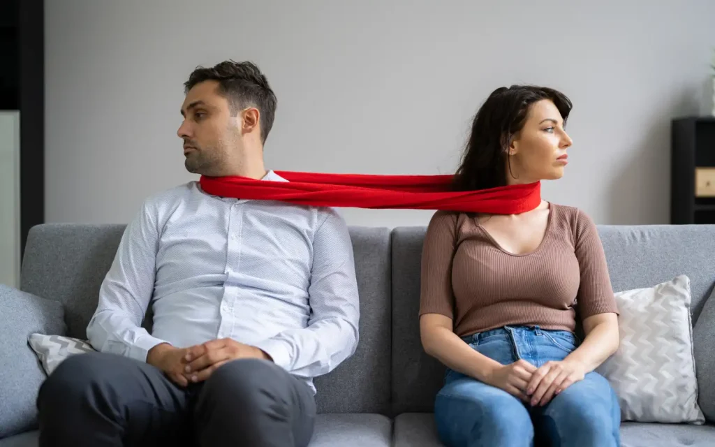 Relationship-patterns-couples-counseling A couple facing away from each other on a couch with material ties round their necks symbolizing negative patterns that can be resolved through relationship counseling