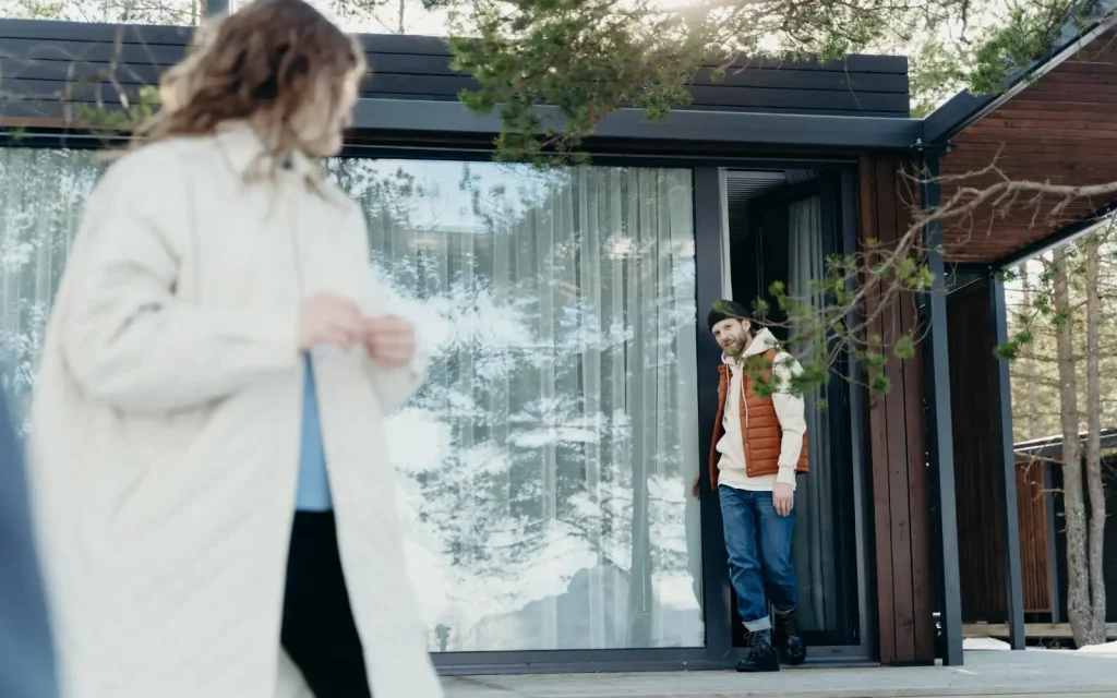 Sound-relationship-house-Gottman-method A woman smiling and turning around outside her house after seeing her partner exiting a door. The partner is making eye contact with the woman symbolizing the Gottman method's sound relationship house.
