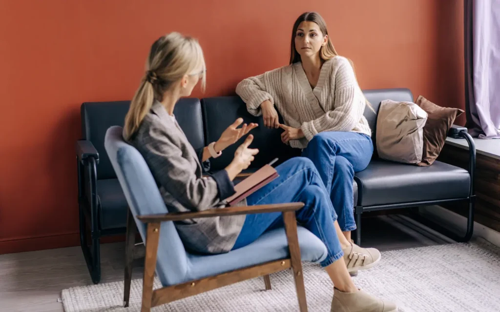 A woman sitting on a couch during a therapy session looking at her therapist as she talks and gestures with her hands