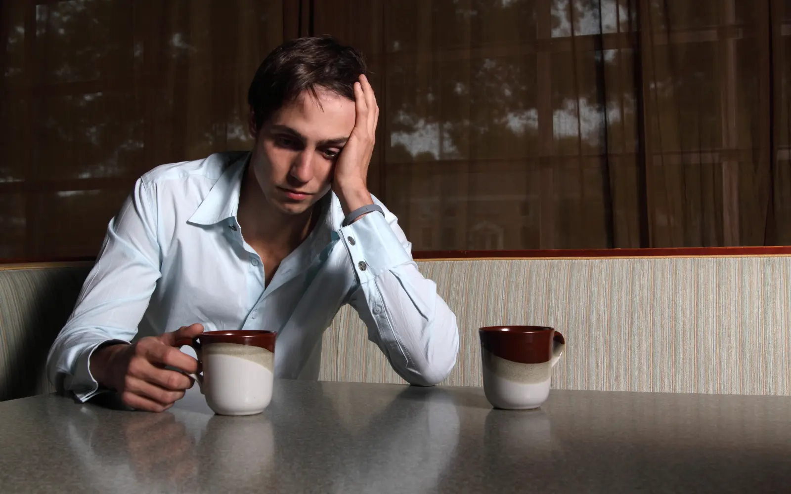 A man staring at a mug of coffee with another mug beside him, representing being lonely in a relationship