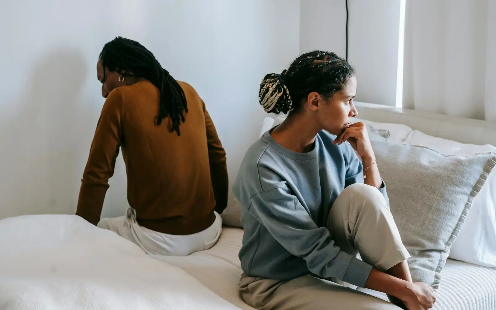 A couple sitting on opposite sides of a bed facing away from each other, representing the kind of relationship difficulties that cause couples to come to couples therapy