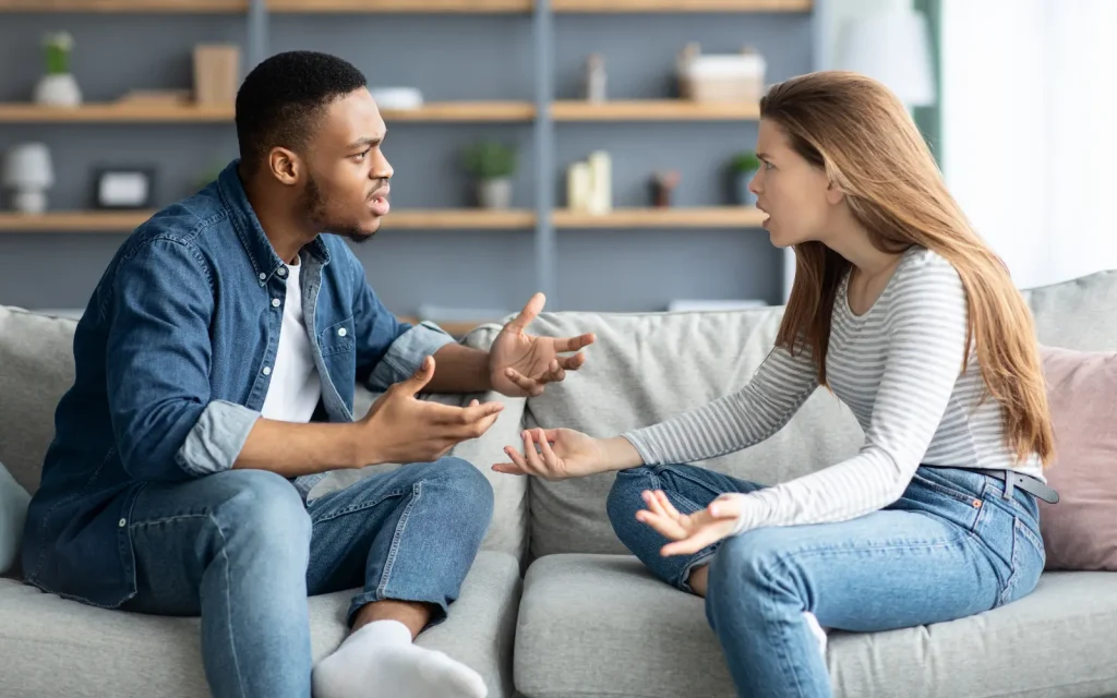 A black man and white woman arguing on a sofa, representing situations many interracial couples face before seeking therapy