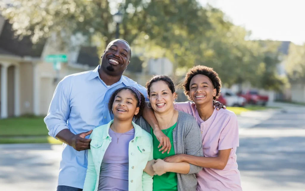 A mixed race family with their arms around each other, smiling and laughing, representing the wider benefits of interracial couples therapy