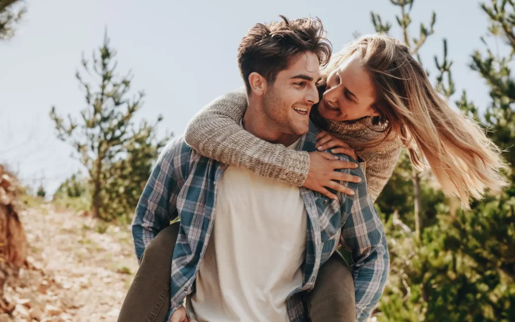 A couple having fun outdoors, the man carrying his partner on his back, representing the end result of successful pre-marital counseling
