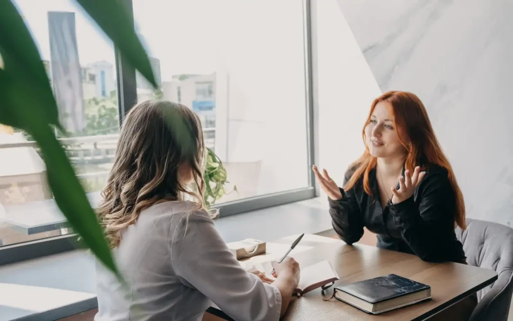 Therapist-note-taking-discussion-with-client A therapist and client sitting across from each other, the therapist taking notes while the client smiles at them after discussing how they feel about note-taking in sessions.