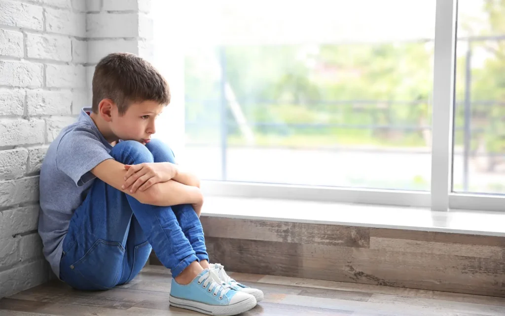 A child sitting on the floor against a wall looking sad, representing childhood wounds that can be uncovered during couples therapy