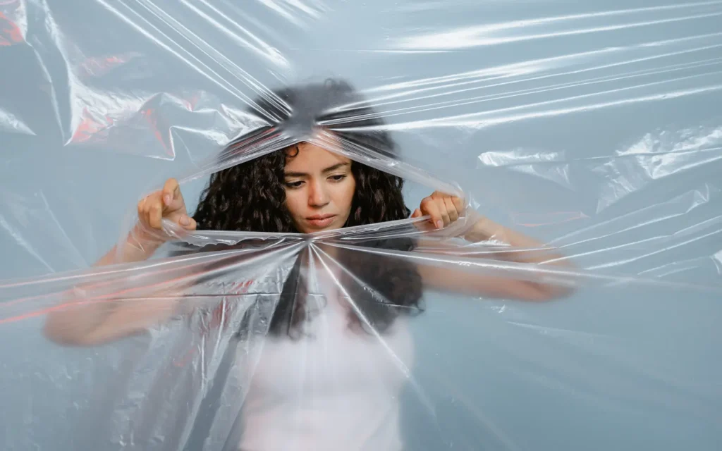 A woman pulling apart a plastic barrier with her hands, representing how therapy can help you break through emotional barriers like excessive crying