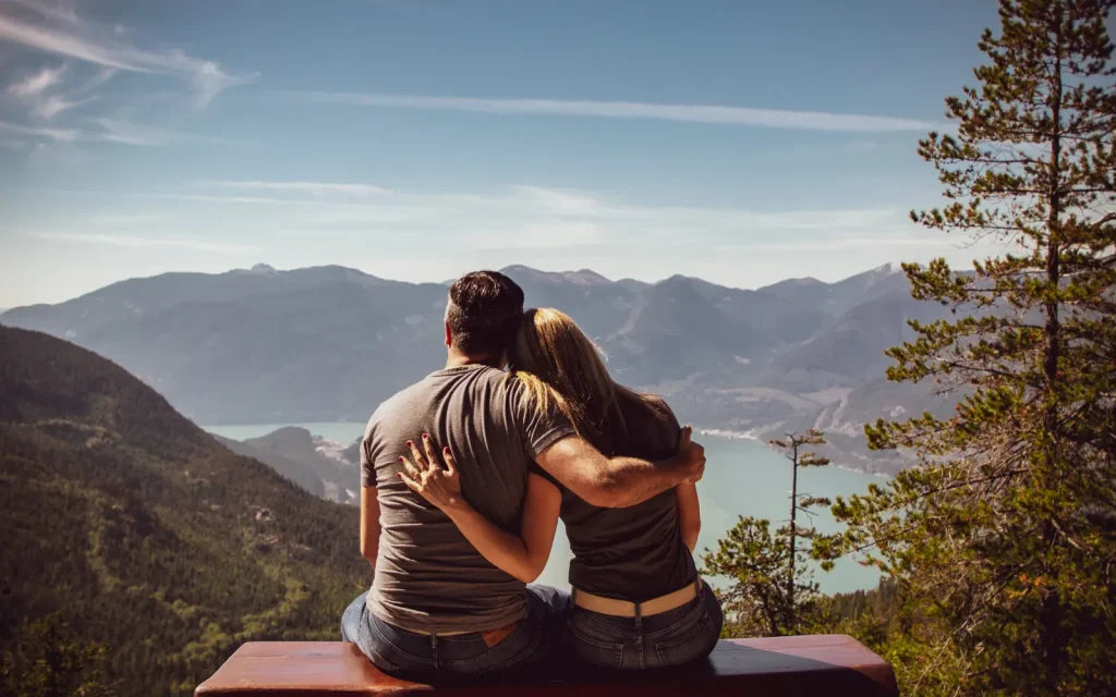 Couple-inviting-connection-in-couples-therapy A couple embracing while viewing a stunning mountain scene, representing connection through couples therapy
