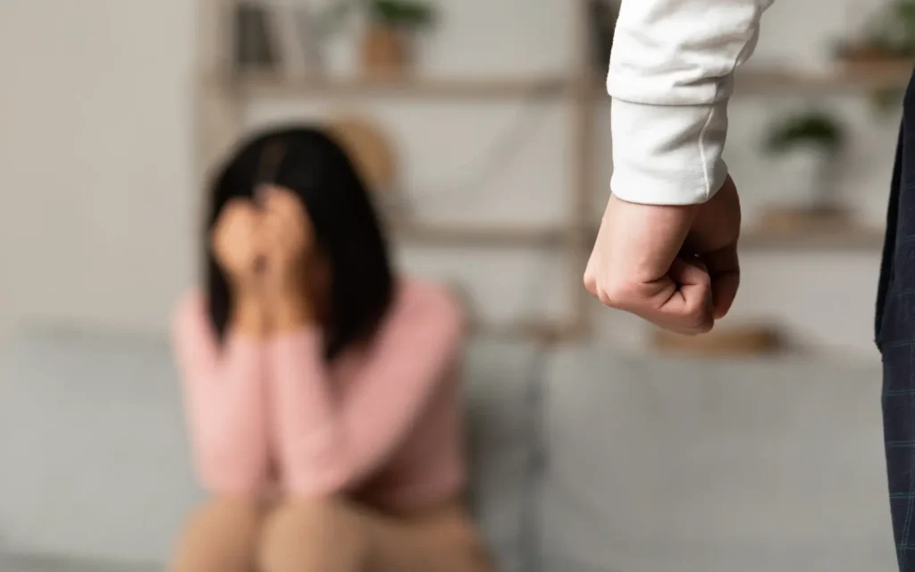 A man with clenched fists standing over a crying woman with her head in her hands, representing domestic violence considerations in couples counseling for narcissists