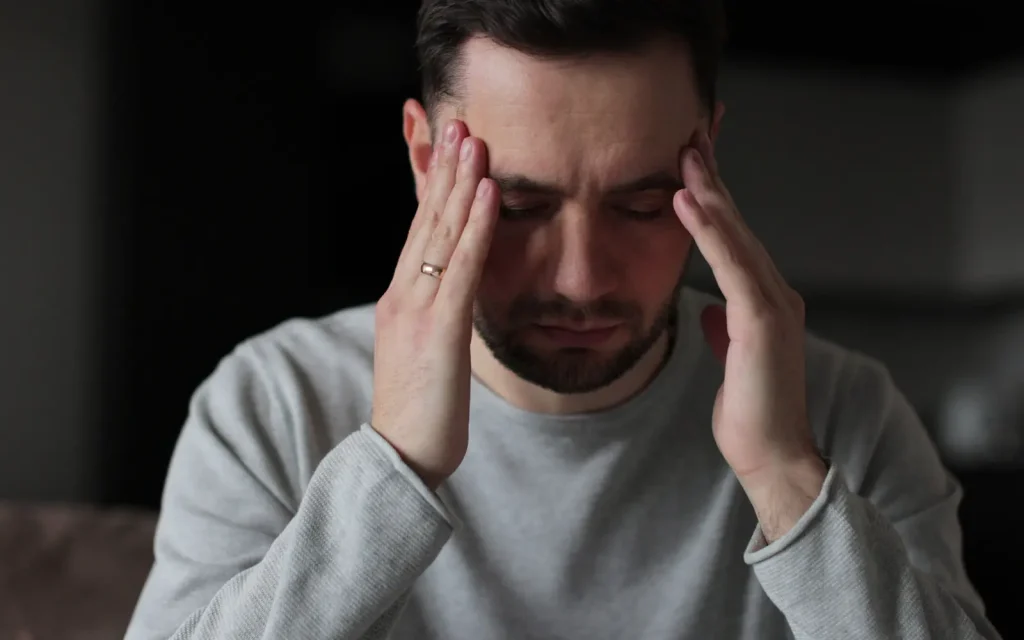 Emotional-processing-in-therapy-LA A man with both hands touching his temples with eyes closed, representing the kind of somatic and emotional processing that can be helpful through individual therapy in Los Angeles