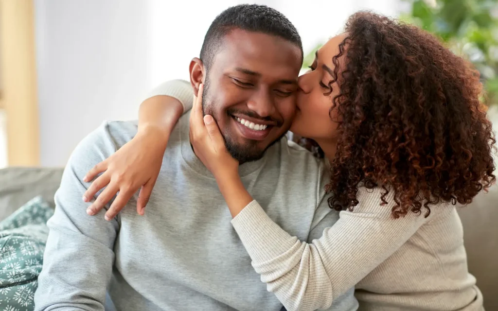 Neurodivergent-couples-therapy A black couple smiling. The woman is kissing the man's cheek, representing the positive impact of love and understanding in couples therapy for neurodivergent individuals