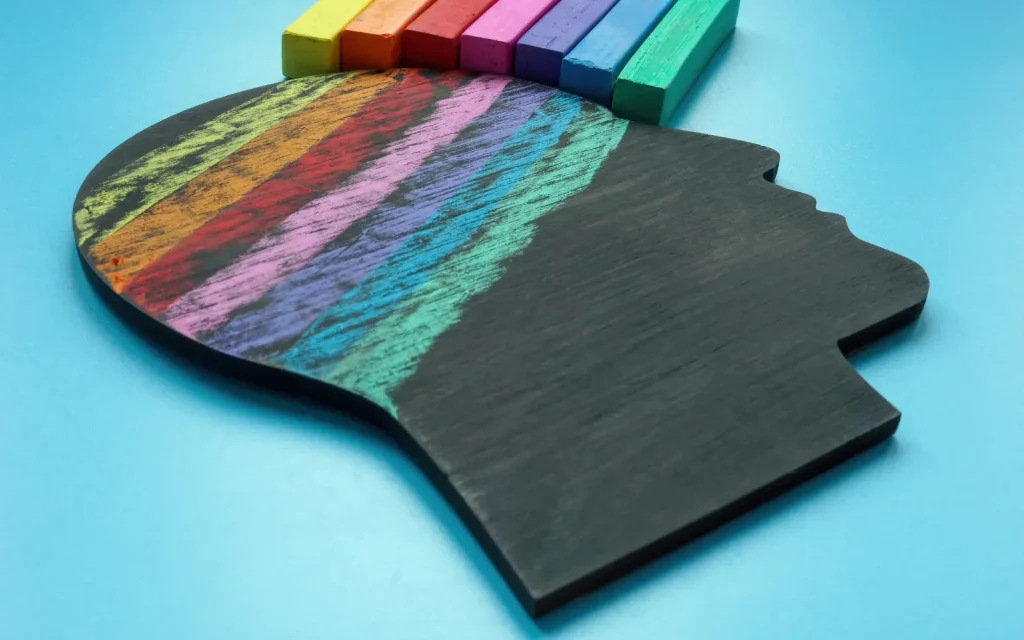 Neurodiverse-therapy-in-LA A black chalkboard in the shape of a human head's silhouette with a chalk rainbow drawn over the brain area, representing neurodiverse therapy in Los Angeles