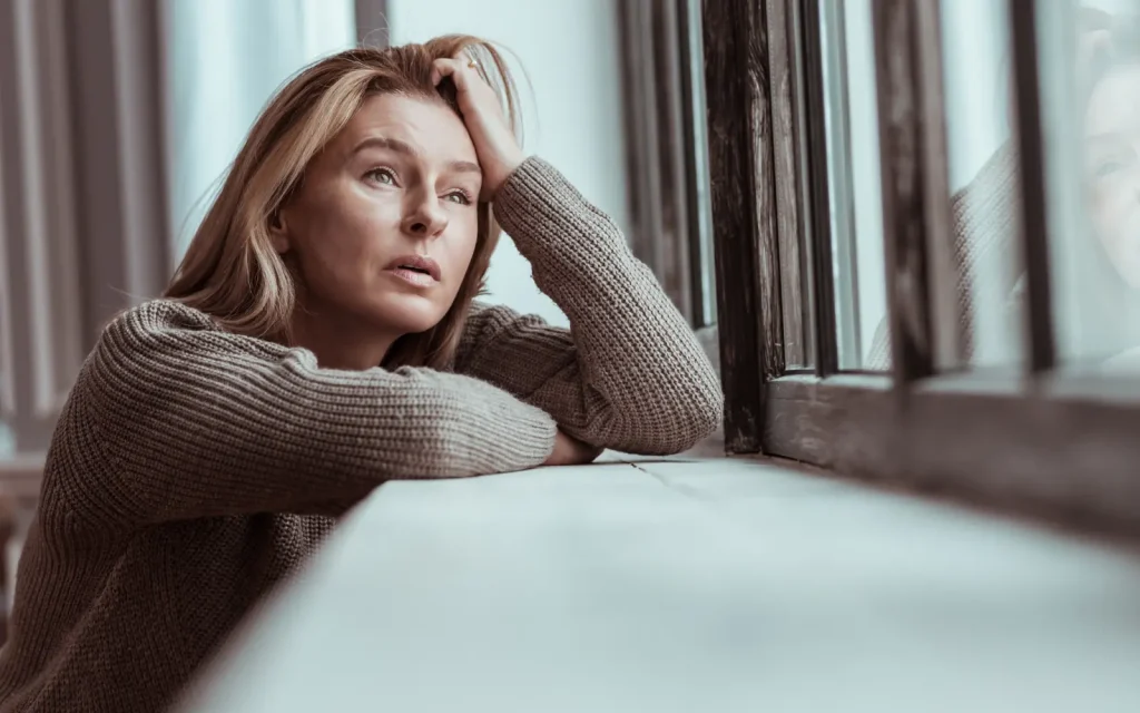 A woman looking out of a window with her head in her hand in despair, representing the importance of safety in couples therapy
