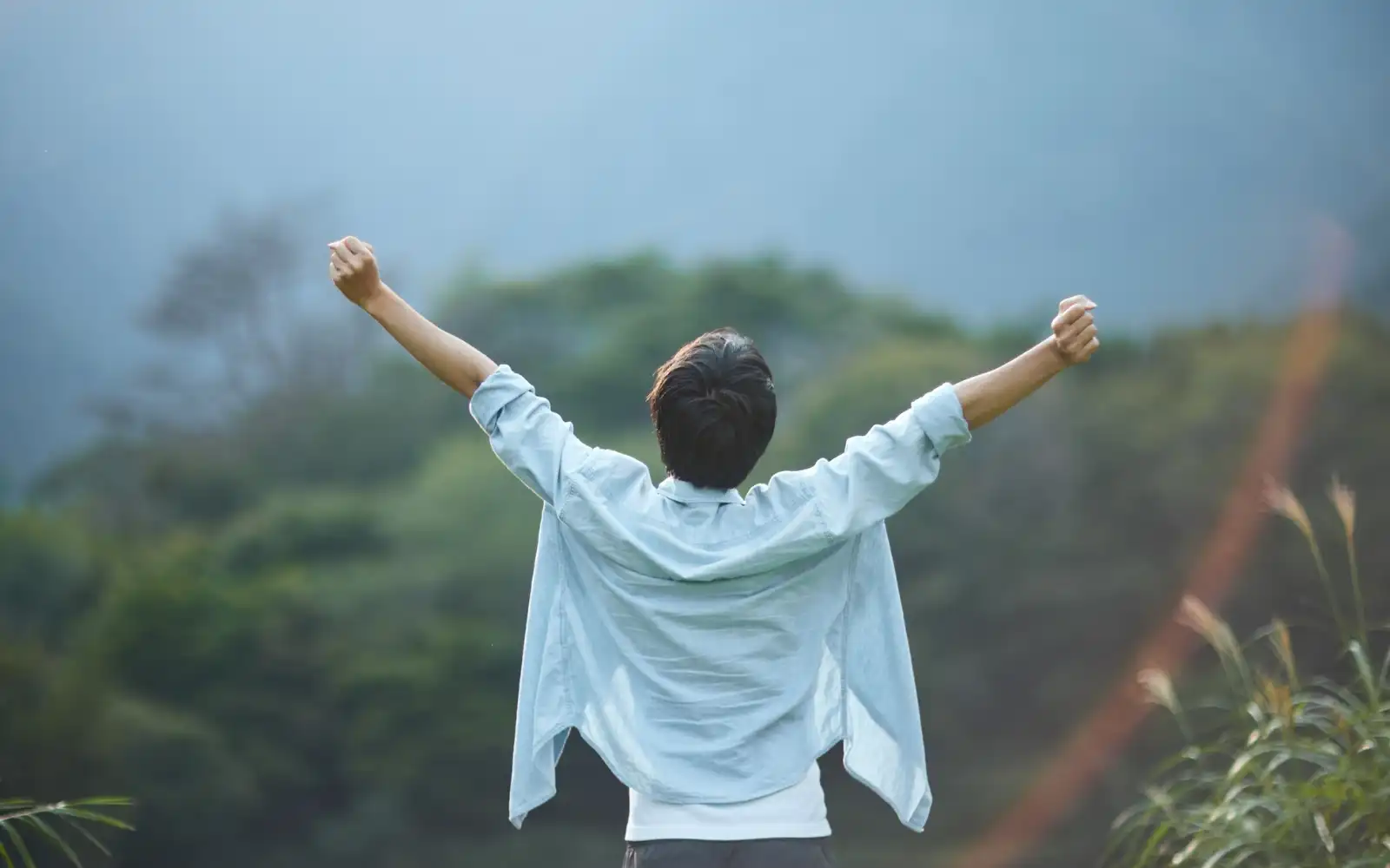 A man standing outside overlooking a mountain with arms raised above his head, representing the freedom that is possible through Los Angeles trauma therapy