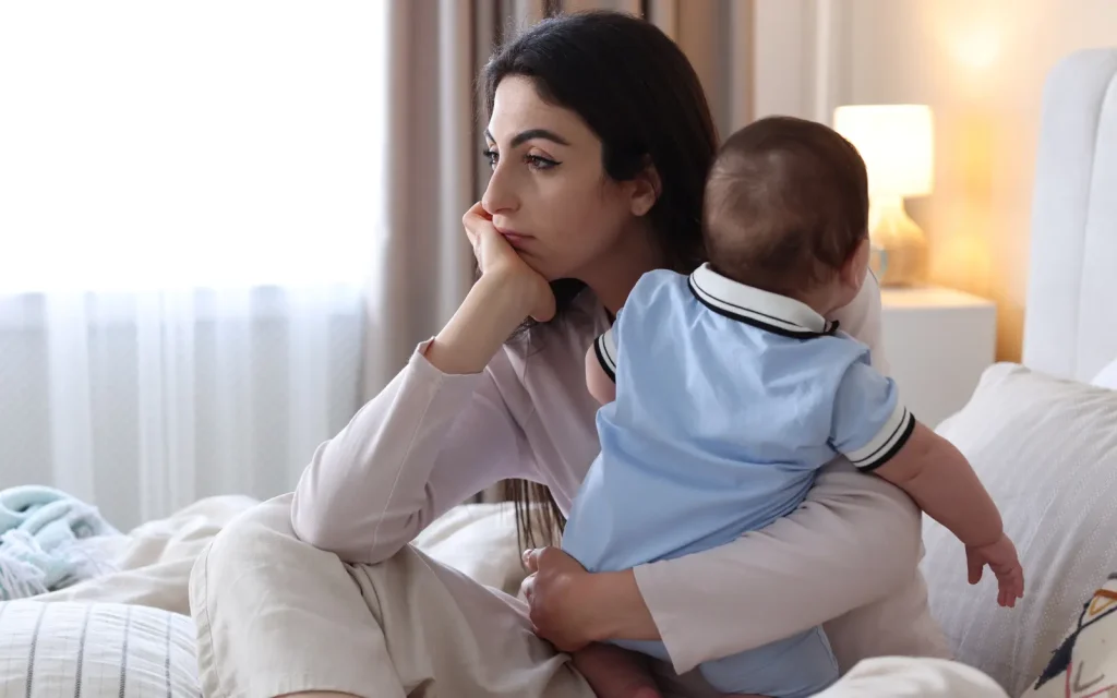 Woman-wanting-to-return-to-work A woman holding a baby and looking pensive, representing the desire of many women to return to the workplace