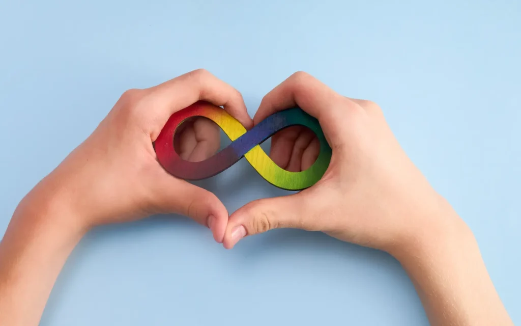 Two hands forming a heart around the international symbol for neurodivergence.
