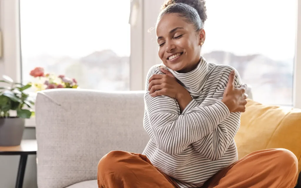 A smiling woman with her arms wrapped around herself, representing self-compassion from GGPA's neurodiverse therapy