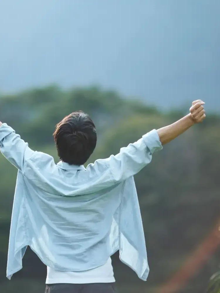 A man standing outside overlooking a mountain with arms raised above his head, representing the freedom that is possible through Los Angeles trauma therapy