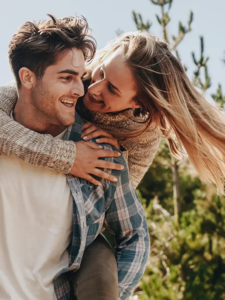 A couple having fun outdoors, the man carrying his partner on his back, representing the end result of successful pre-marital counseling