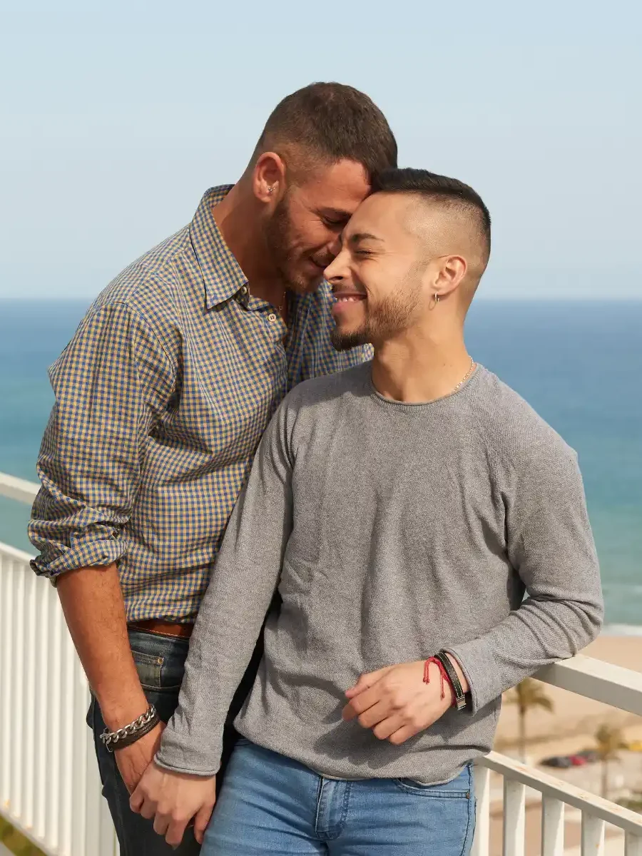 A happy LGBTQ+ couple shares an intimate moment on a scenic balcony overlooking the ocean. The image conveys love, connection, and emotional closeness, symbolizing the benefits of LGBTQ couples therapy in strengthening relationships.