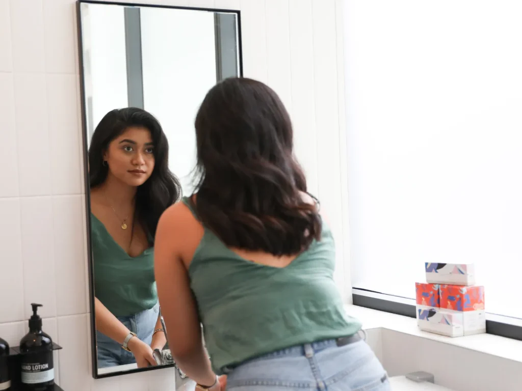 A woman looking at herself in the mirror, representing confidence & self talk