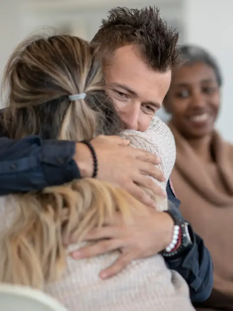 A couple hugging in front of their therapist when graduating EFT therapy and reflecting on their past sessions and journey