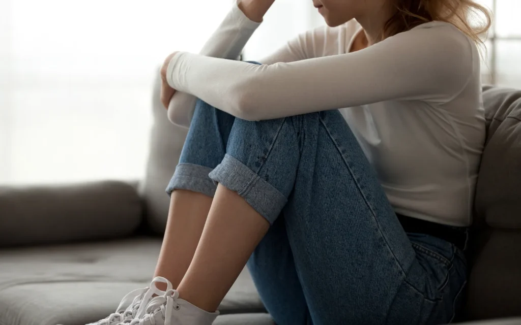 A woman sitting on a sofa visibly distressed, representing anxiety that causes paralysis in women