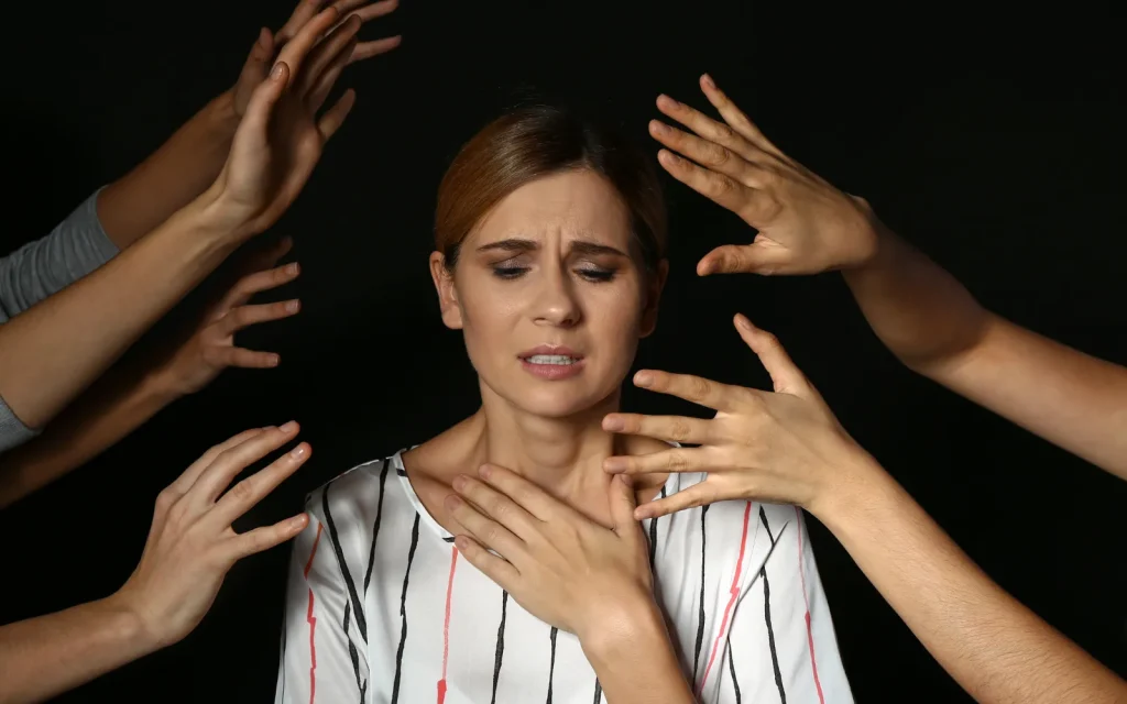 A woman holding her chest surrounding by grasping hands, representing feeling overwhelmed by anxiety